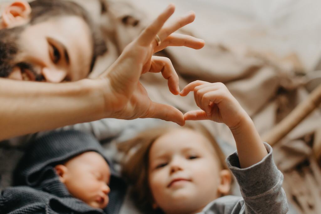 Kinderhände und Elternhände formen gemeinsam ein Herz über einem schlafenden Baby