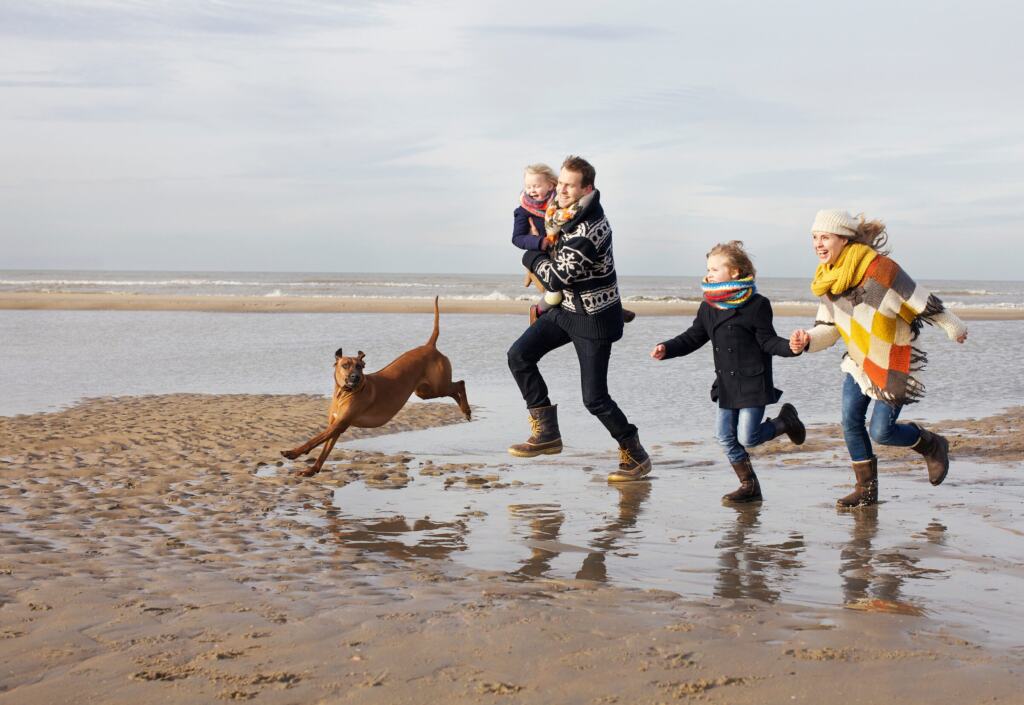 Familie läuft mit ihrem Hund über den weiten Sandstrand bei Ebbe