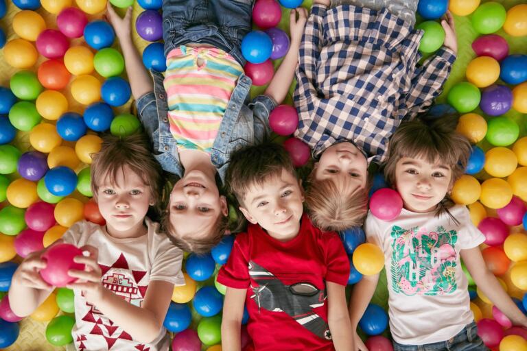 Fünf Kinder liegen lachend im Kreis in einem bunten Bällebad