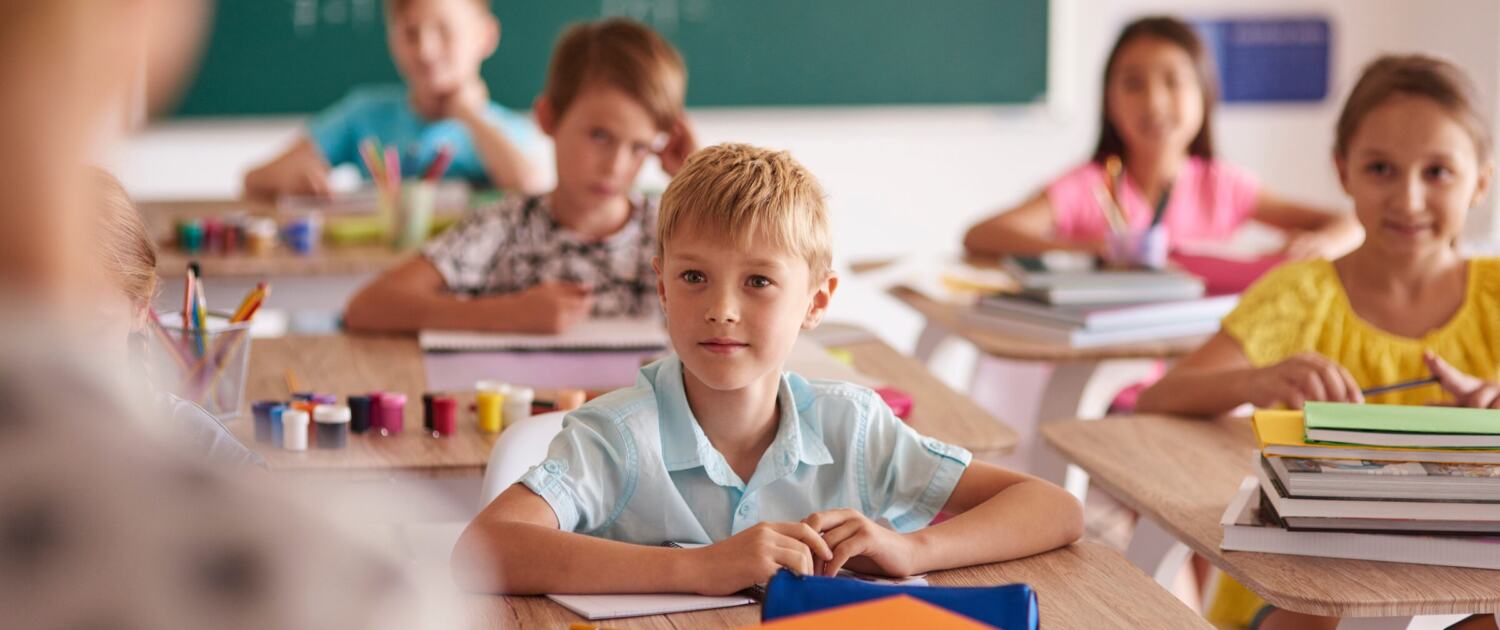 Kinder sitzen an ihren Pulten in einem hellen Klassenzimmer und arbeiten konzentriert