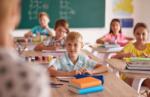 Kinder sitzen an ihren Pulten in einem hellen Klassenzimmer und arbeiten konzentriert