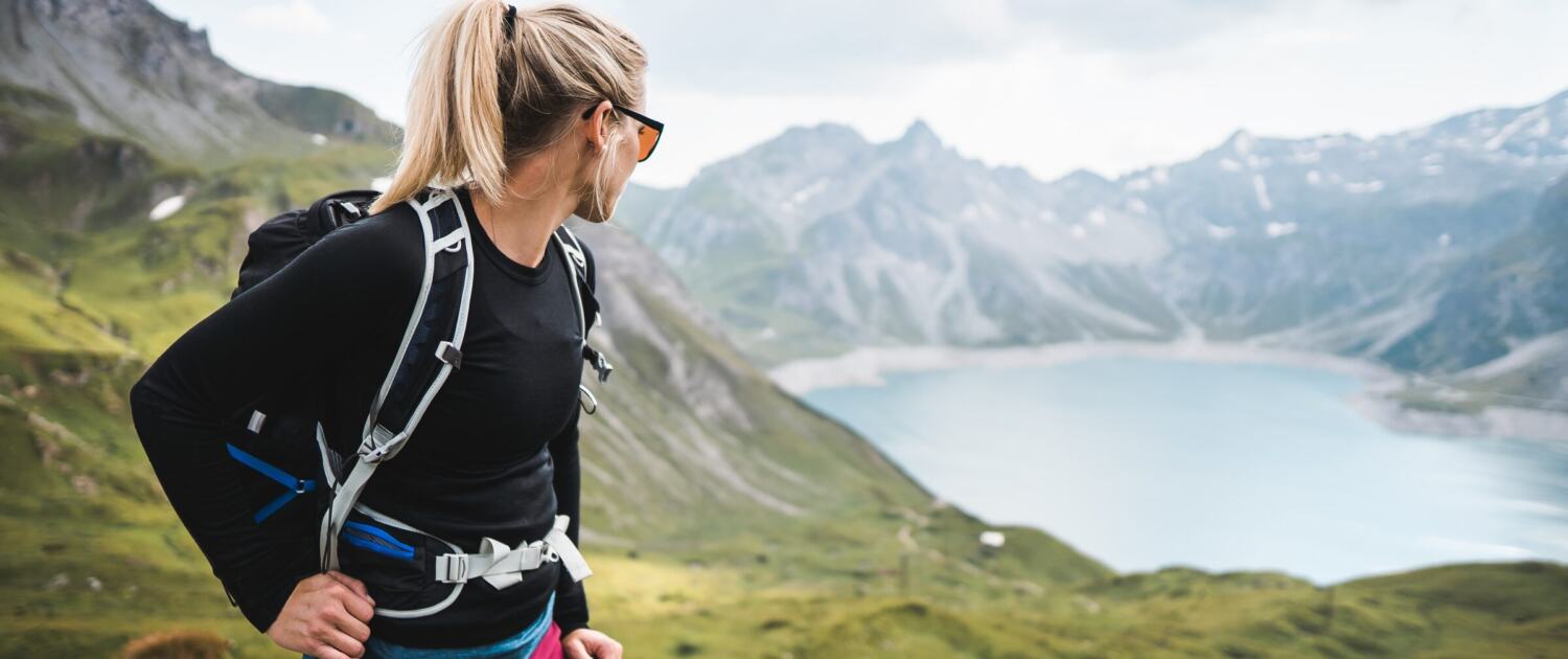 Frau mit Rucksack blickt bei einer Wanderung auf einen Bergsee in den Alpen